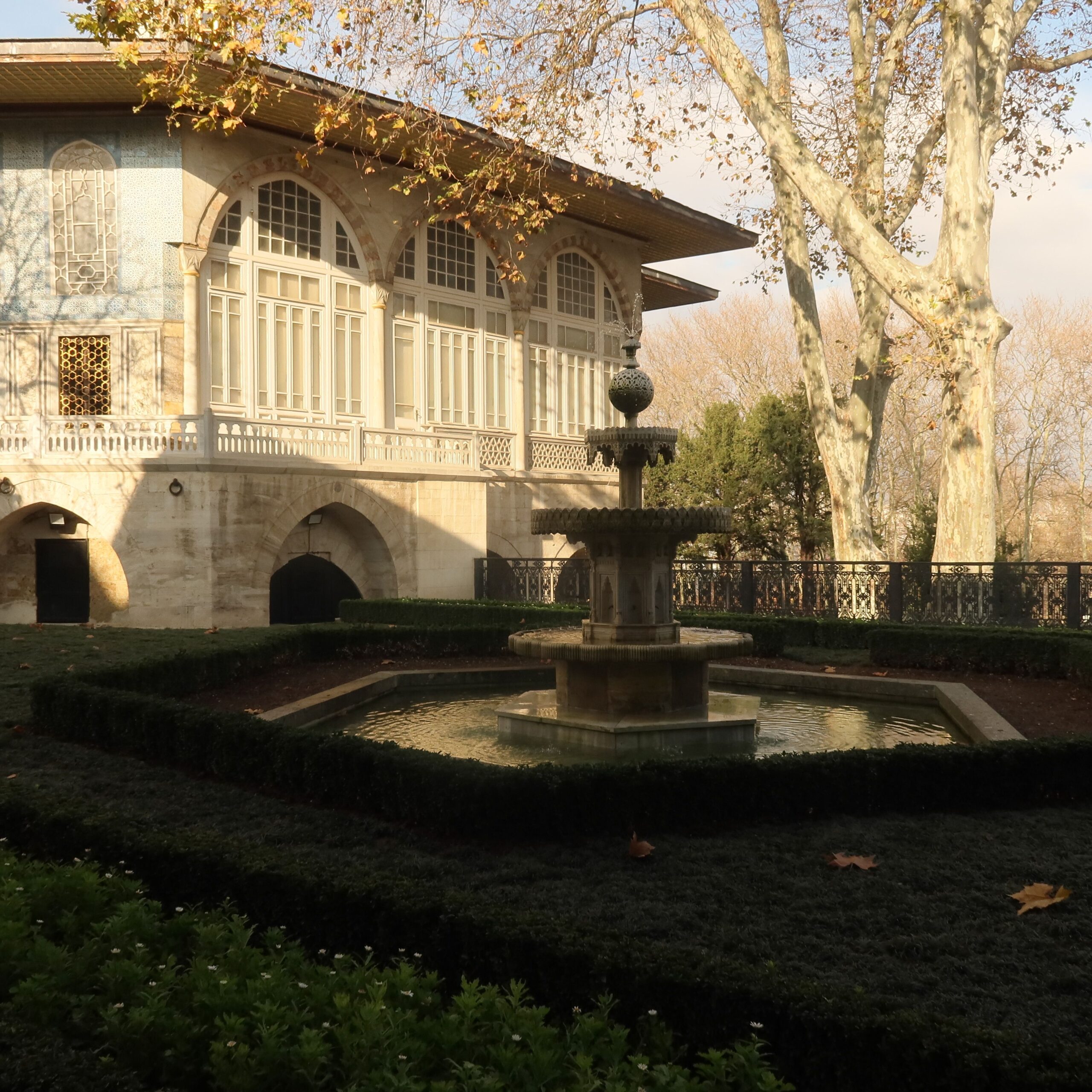 Serene garden view with a historical mansion and fountain under autumn skies.
